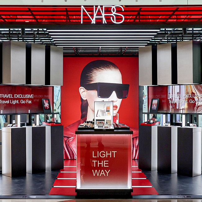 A modern, minimalist NARS pop-up store showcasing Altavia's innovative retail design. The space features a striking red accent wall, a large product display, and impactful visual elements highlighting the "Light The Way" campaign.